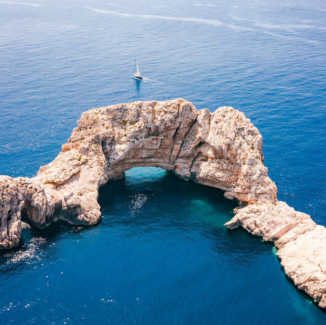 Aerial view of a natural rock arch and a sailing boat, the kind of view our scenic helicopter tours offer